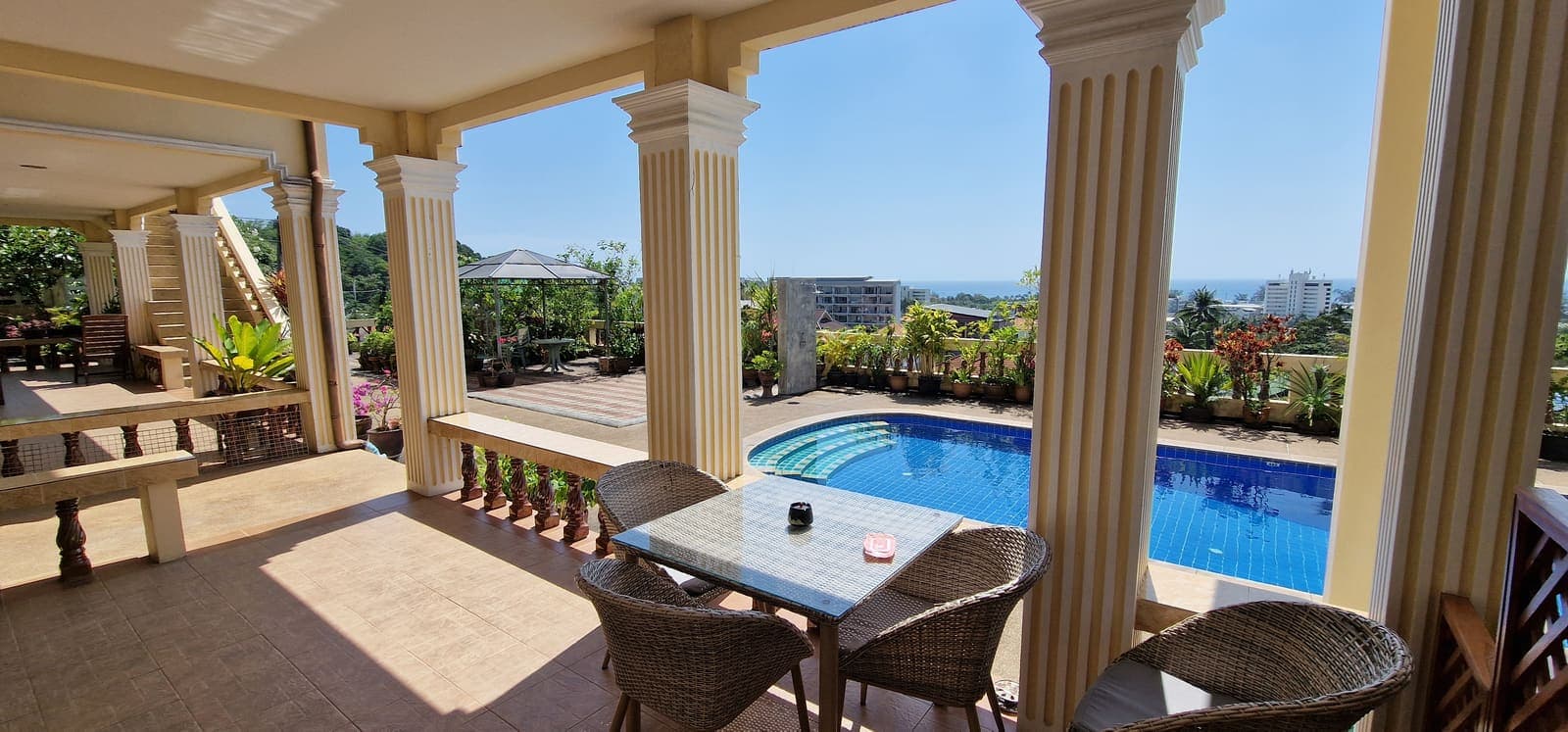 Covered terrace with dining table, columns, pool and sea view